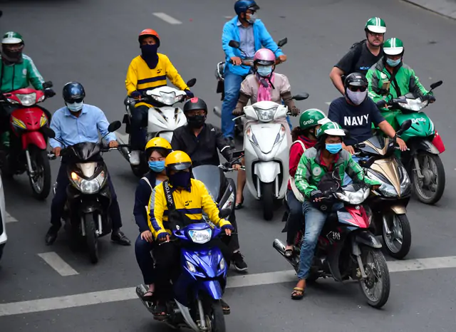 Motorbike riders, including ride-hailing drivers, waiting at an intersection in Vietnam